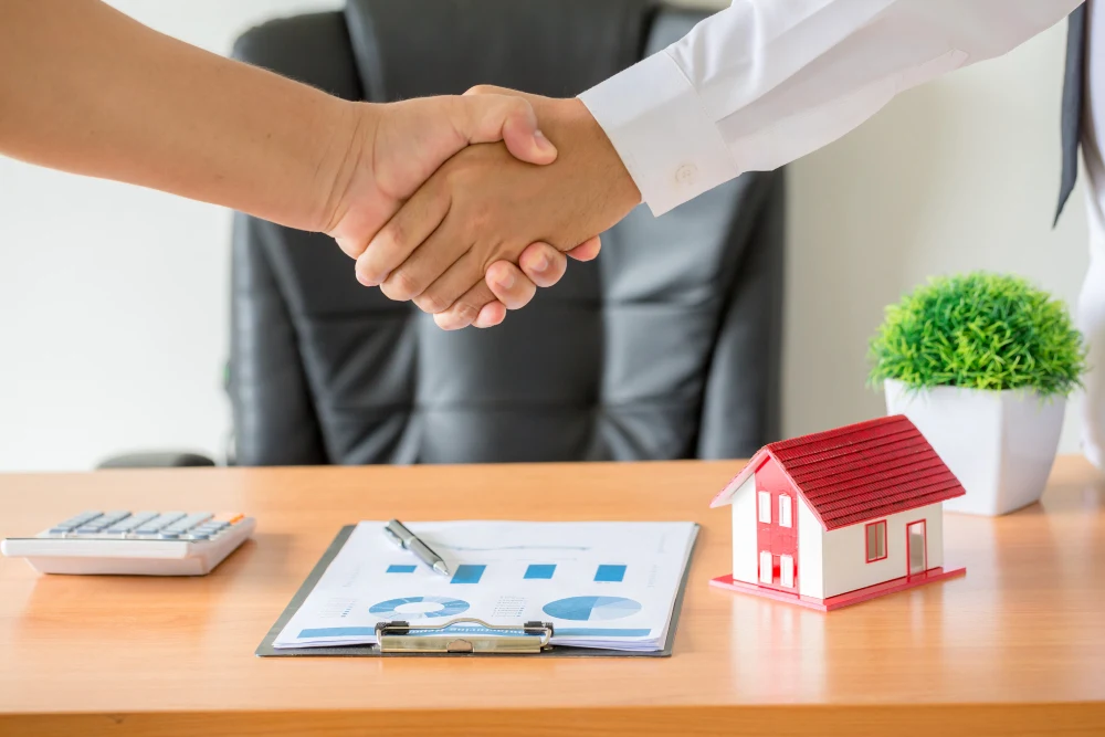 Handshake Over Desk with Financial Documents and Small House Model
