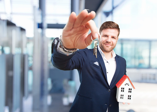 Man in Suit Holding Keys and Small House Model in Office